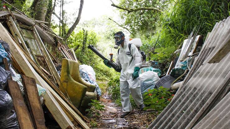 foto de um homem em meio as entulhos colocando veneno de mosquito da dengue