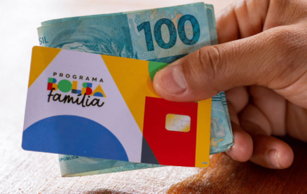 Mão segurando cédulas de 100 e cartão do Bolsa Família