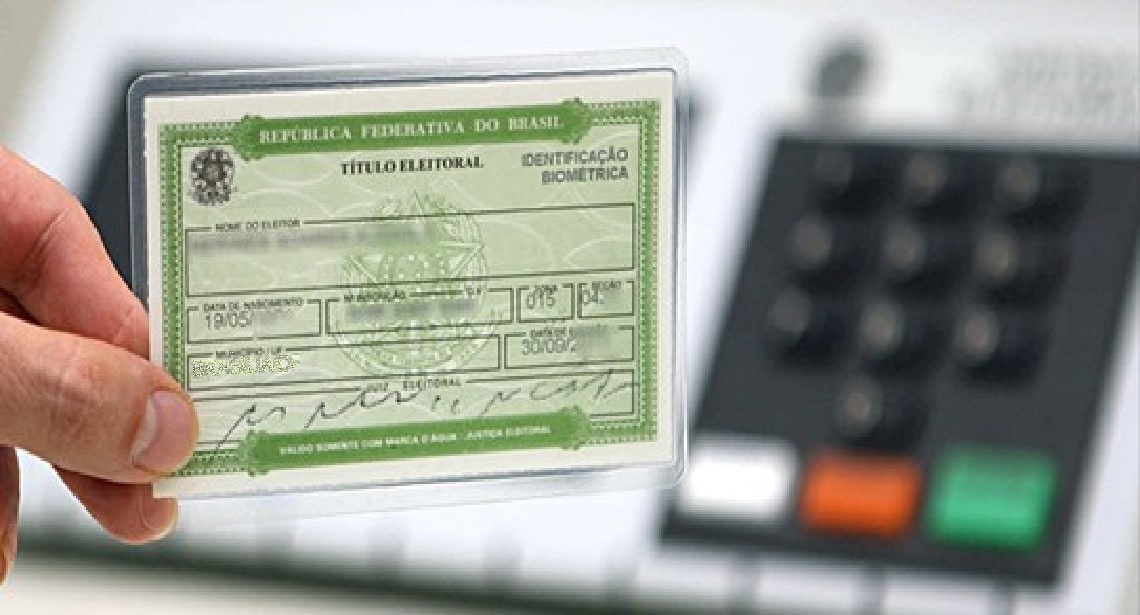 Mão segurando título de eleitor em frente a urna