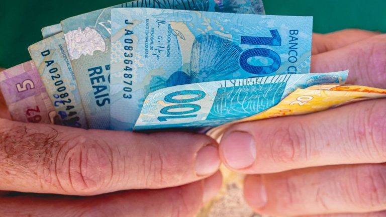 mão segurando notas de dinheiro de 100 reais