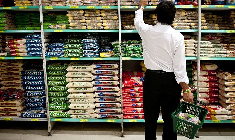 Homem no supermercado verificando o preço do arroz e feijão
