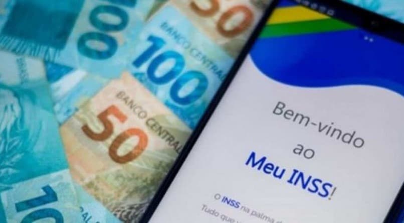 tela do celular aberta no site do inss e rodeado de dinheiro