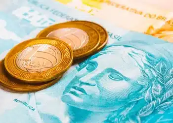 moedas de um real em cima de uma nota de 100 reais para representar o pagamento antecipado do inss
