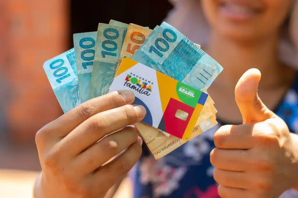 mulher segurando dinheiro e cartão do Bolsa Família