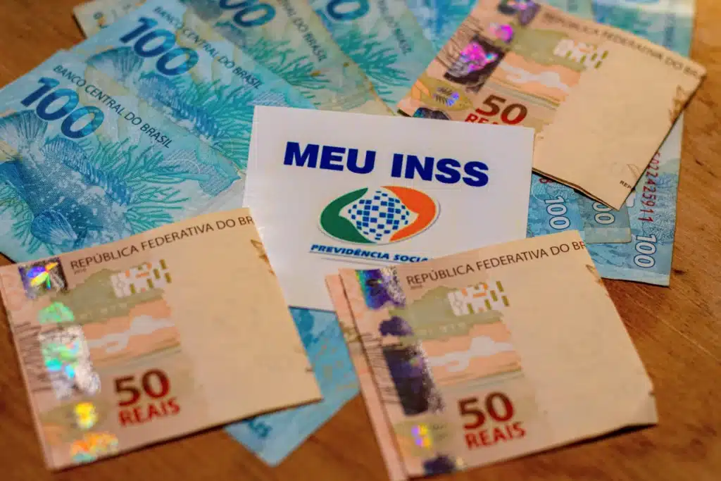 várias notas de 100 e 50 reais ao lado do cartão do inss