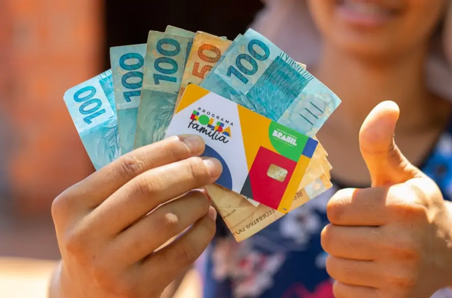 mulher com o pagamento do bolsa família em mãos, juntamente com o cartão do benefício