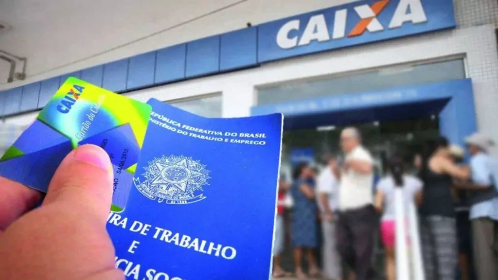 pessoa segurando carteira de trabalho. ao fundo agência da caixa com fila grande.