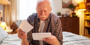 idoso com ar de triste, conferindo papéis, sentado numa cama
