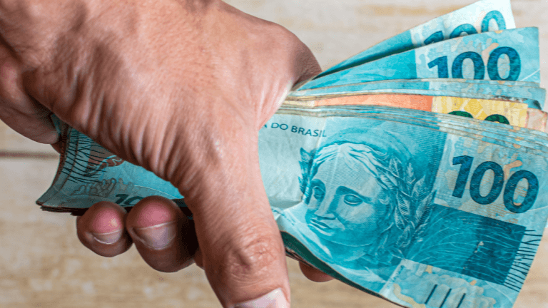 mão segurando várias notas de 100 reais
