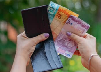mão com as unhas pintadas segurando uma carteira com notas de 100, 20 e 5 reais