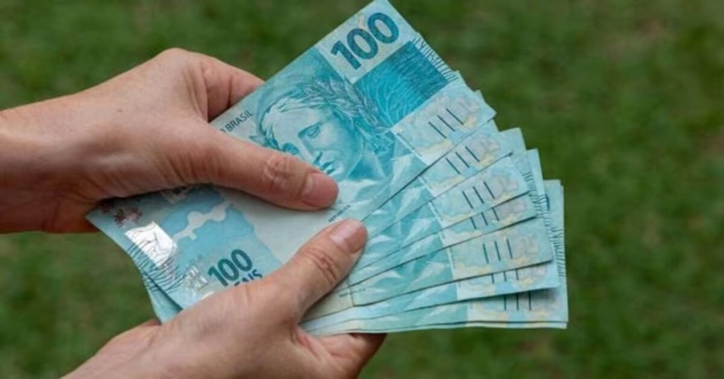 mão segurando várias notas de 100 reais
