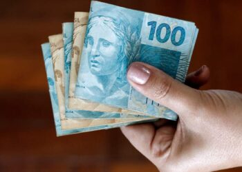 mãos segurando notas de dinheiro que caem em conta quando o INSS paga aposentadoria em dobro