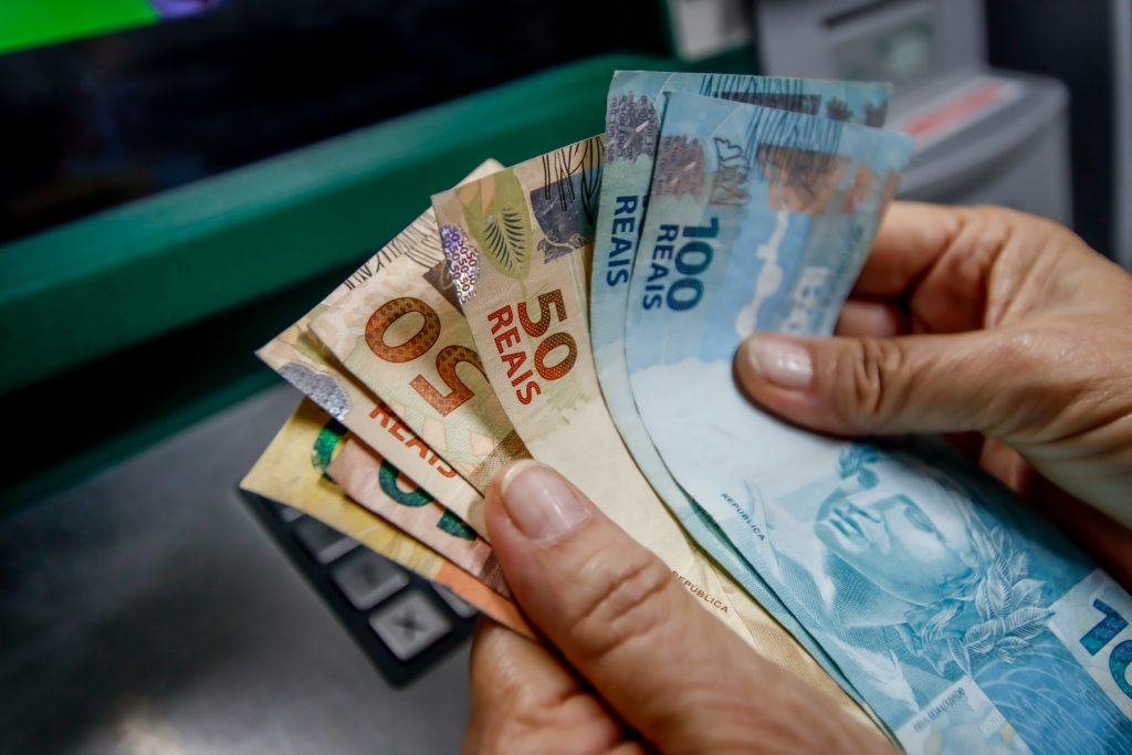 mão no caixa eletrônico sacando notas de 100 e 50 reais referentes ao pagamento do inss