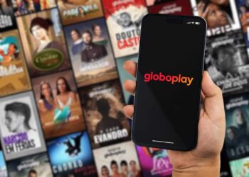 mão segurando o celular aberto na globoplay com todos os catálogos de novela de fundo