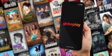 mão segurando o celular aberto na globoplay com todos os catálogos de novela de fundo