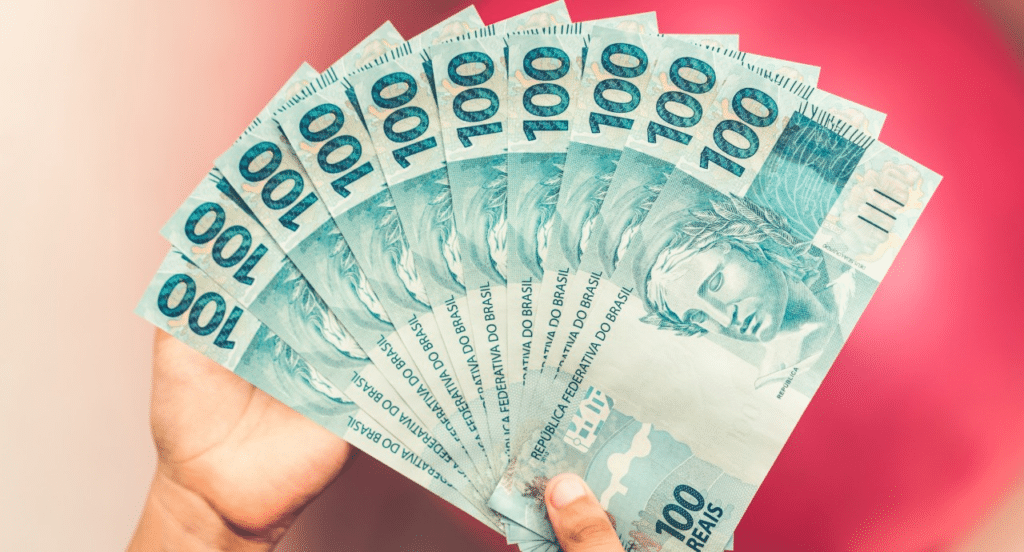 Leque com notas de R$100 em fundo cor de rosa