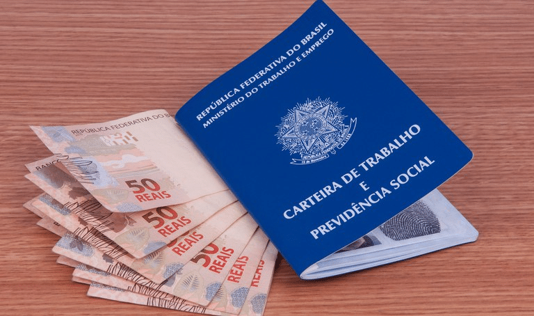 Carteira de trabalho com notas de R$50 ao lado