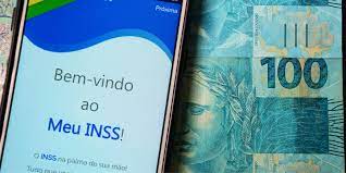 celular aberto na tela do INSS ao lado de uma nota de 100 reais