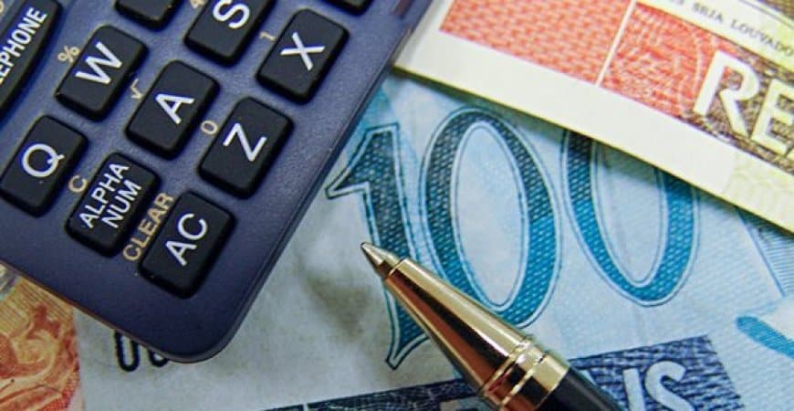 calculadora ao lado de caneta e dinheiro fazendo conta das dívidas