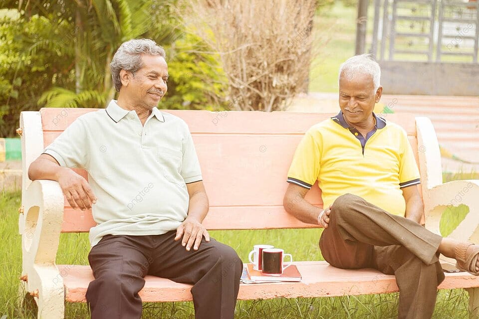 dois aposentados do INSS sentados em um banco de praça, conversando e bebendo café em uma tarde ensolarada
