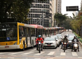 vários transportes públicos no meio da avenida e ao lado de carros
