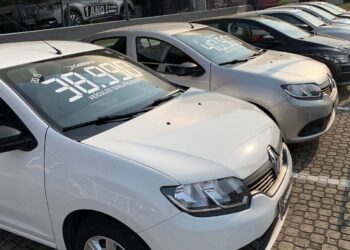 carros enfileirados. o primeiro é um pegeaut branco e possui em seu parabrisa o valor 38.990 escrito em branco