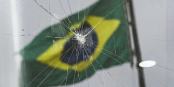 Imagem de um vidro quebrado com a Bandeira do Brasil ao fundo (Fonte: Reprodução/Agência Brasil)