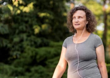 mulher branca aparentando ter uns 50 anos, ao ar livre, caminhando, usando fones de ouvido com fio