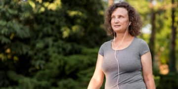 mulher branca aparentando ter uns 50 anos, ao ar livre, caminhando, usando fones de ouvido com fio