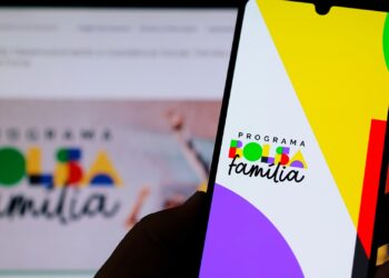 imagem de uma pessoa segurando o celular com o logo do Bolsa Família e Auxílio Gás