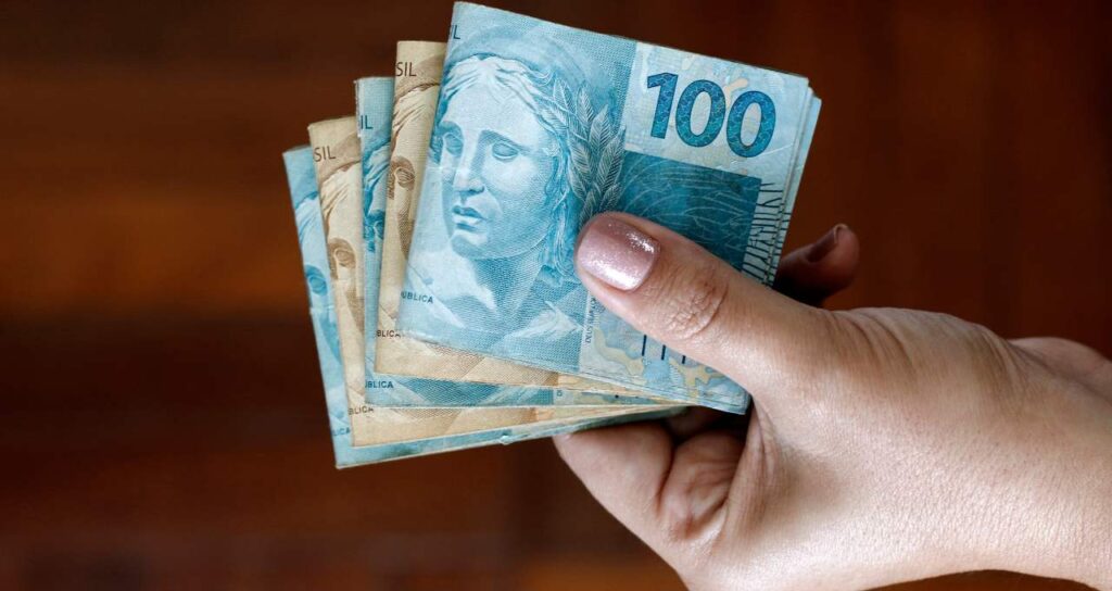imagem de uma mão segurando o dinheiro do salário mínimo)