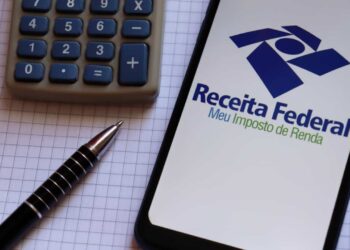 foto de celular com site da receita federal aberto sobre uma toalha quadriculada. ao lado está uma calculadora e uma caneta preta