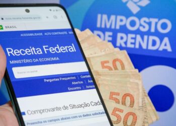 mão segurando celular com site da receita federal aberto e algumas notas de 50 reais