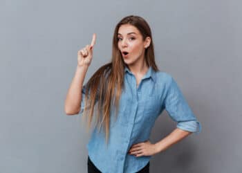 mulher jovem usando camisa azul apontando para cima com a boca aberta