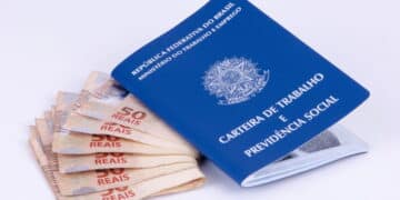 Pagamento de dinheiro extra pra quem é CLT: cédulas de 50 reais ao lado de uma carteira de trabalho. (Fonte: depositphotos).