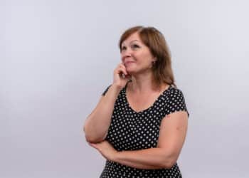 Mulher de meia idade com mão sobre o queixo, aparentando estar com dúvidas