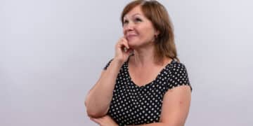 Mulher de meia idade com mão sobre o queixo, aparentando estar com dúvidas