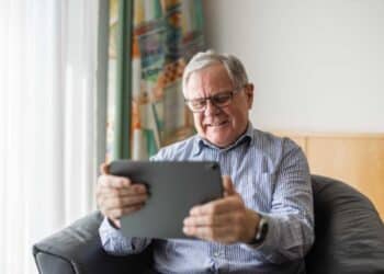 Aposentado sentado na poltrona e lendo notícias no notebook sobre a revisão da vida toda do INSS. (Fonte: shutterstock).