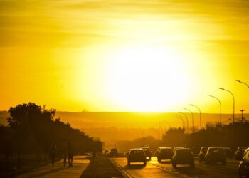 Trânsito na cidade com vários carros e pedestres no horário de verão com céu ensolarado. (Fonte: Revista Amanhã).