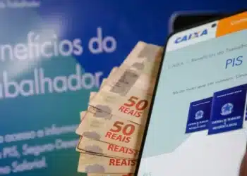 celular aberto no site da caixa para sacar o pis pasep, ao lado de cédulas de 50 reais
