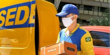 funcionário do correios uniformiazado segurando encomenda em frente caminhão da empresa
