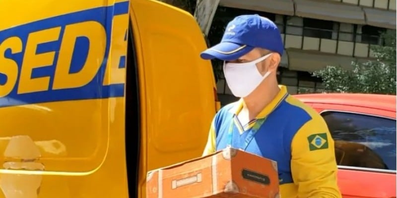 funcionário uniformizado do correios segurando encomenda em frente o caminhão da empresa