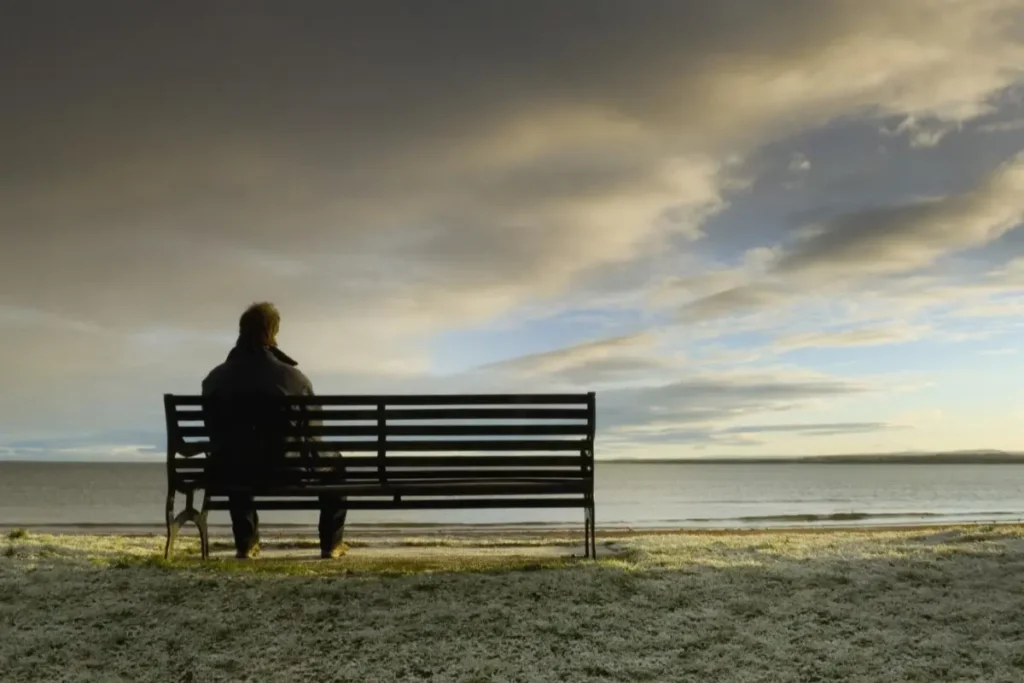homem sozinho, sentado num banco, contemplando o mar