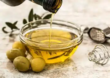 Azeite de oliva sendo despejado em um recipiente de vidro, ao lado de azeitonas. (Fonte: pixabay).