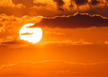 sol bem forte entre as nuvens, com fundo alaranjado e vermelho