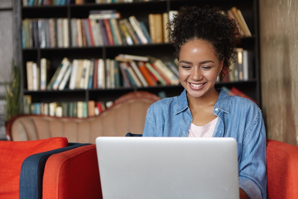 mulher negra usando laptop. ao fundo há uma estante de livros. (Fonte: Reprodução Freepik)