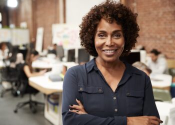 mulher negra, em torno dos 50 anos, com os braços cruzados a frente do corpo, sorrindo. (Fonte: Vagas Profissões)