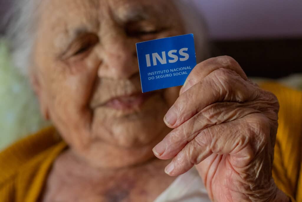 Aposentada segurando cartão do benefício, cabisbaixa e triste com o desconto indevido do INSS. (Fonte: depositphotos).