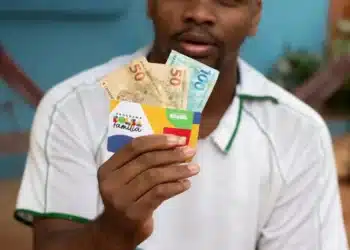 homem negro segurando cartão do bolsa família e notas de 100 e 50 reais