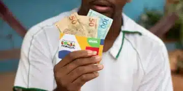 homem negro segurando cartão do bolsa família e notas de 100 e 50 reais